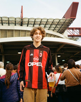 Customer wearing a red and black AC Milan shirt outside a stadium.